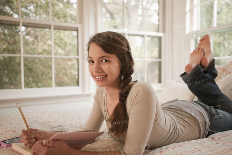 Mixed race girl laying in bed writing in journal
