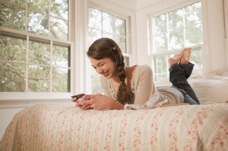 Mixed race girl laying in bed text messaging on cell phone