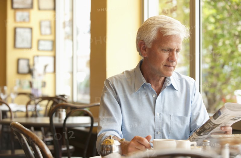 Caucasian man reading newspaper in restaurant