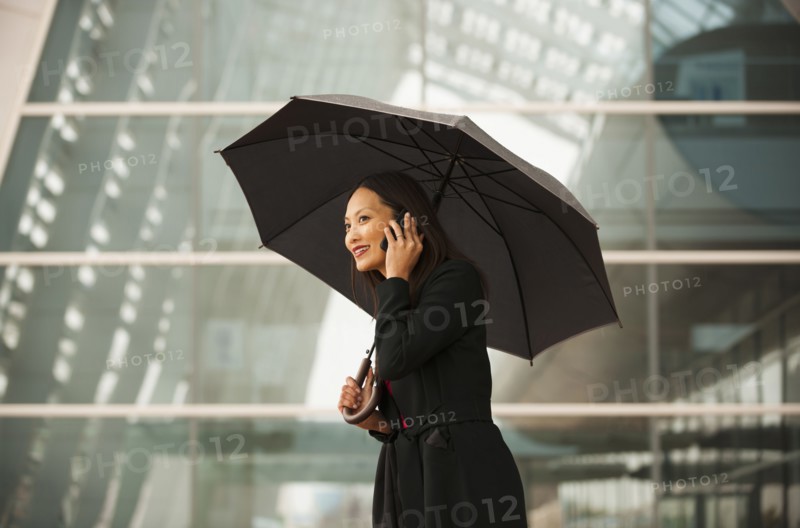 Asian businesswoman with umbrella talking on cell phone
