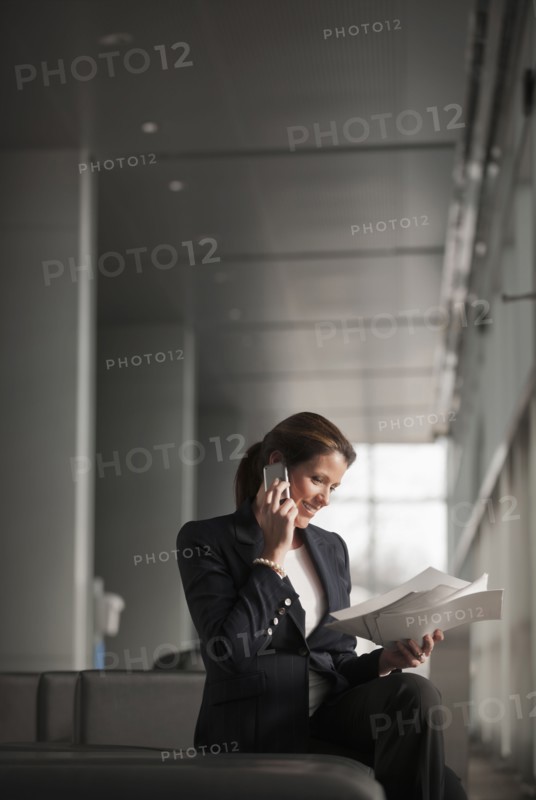 Caucasian businesswoman holding paperwork and talking on cell phone