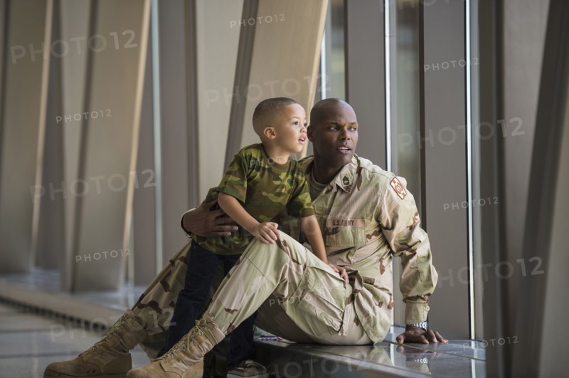 African American soldier and son looking out airport window