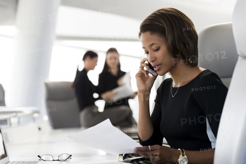 Businesswoman reading paperwork talking on cell phone