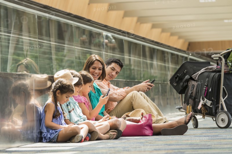 Family waiting on floor of airport using cell phones