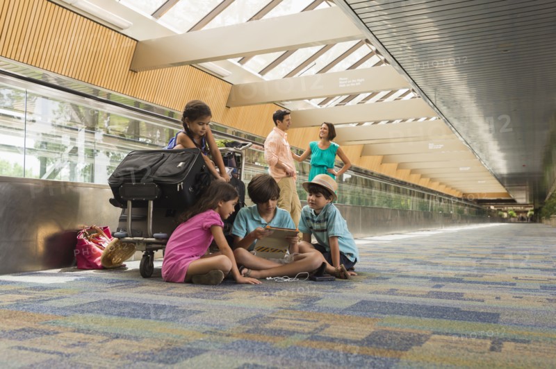 Children waiting in airport with family and using digital tablet