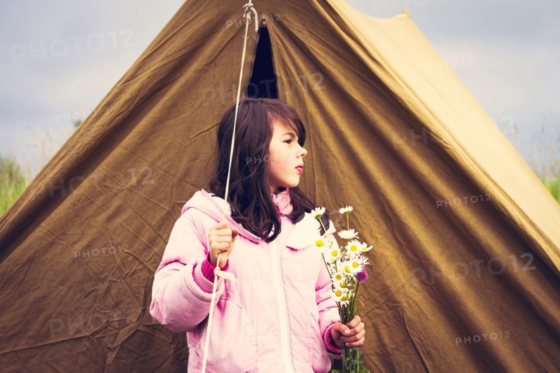 Caucasian girl holding wildflowers near camp tent