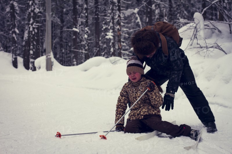 Caucasian father helping cross-country skiing daughter falling in snow