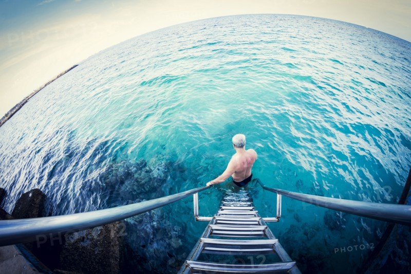 Fish-eye lens view of older Caucasian man descending ladder into ocean
