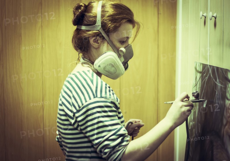 Artist in gas mask airbrushing painting in studio