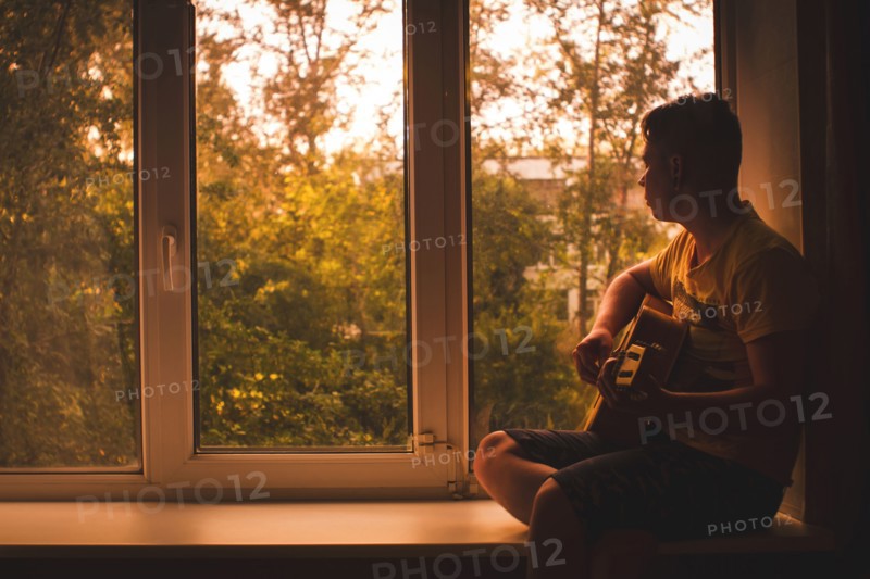 Caucasian man playing guitar in window sill