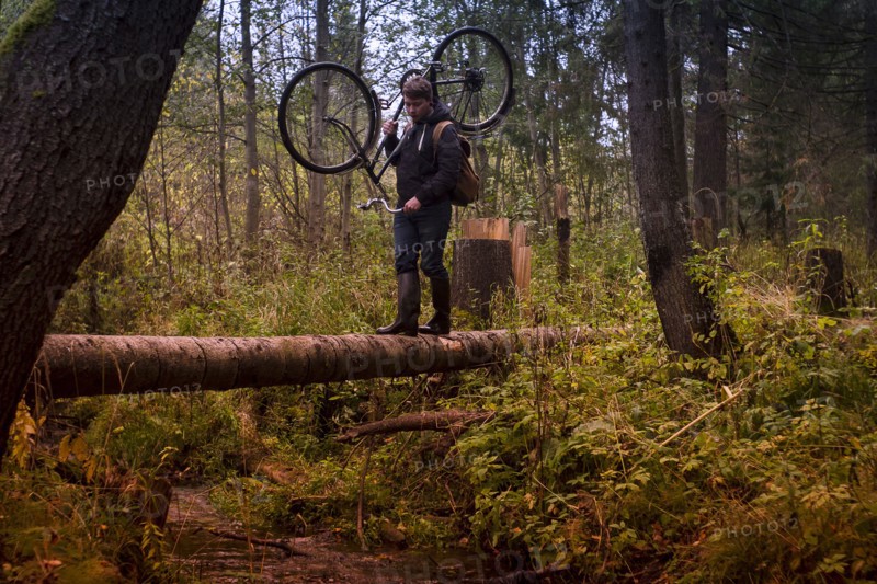 Caucasian man carrying bicycle on fallen tree