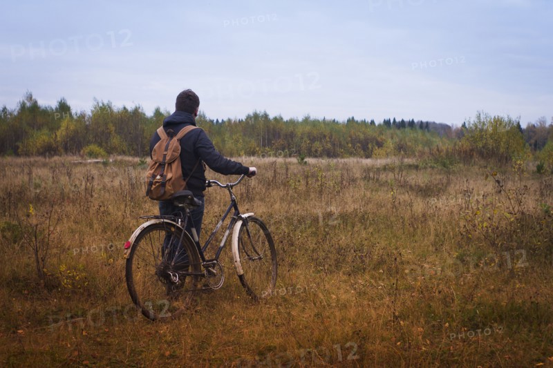 Caucasian man pushing bicycle in field