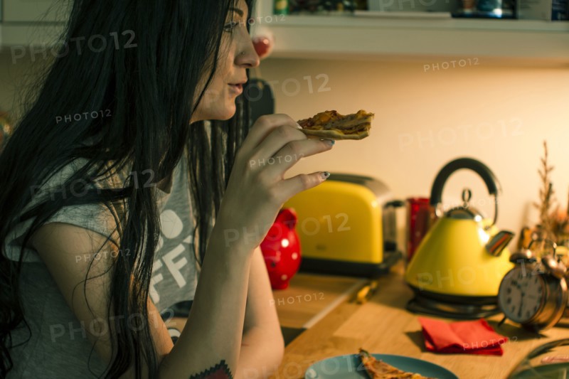 Caucasian woman eating pizza in kitchen