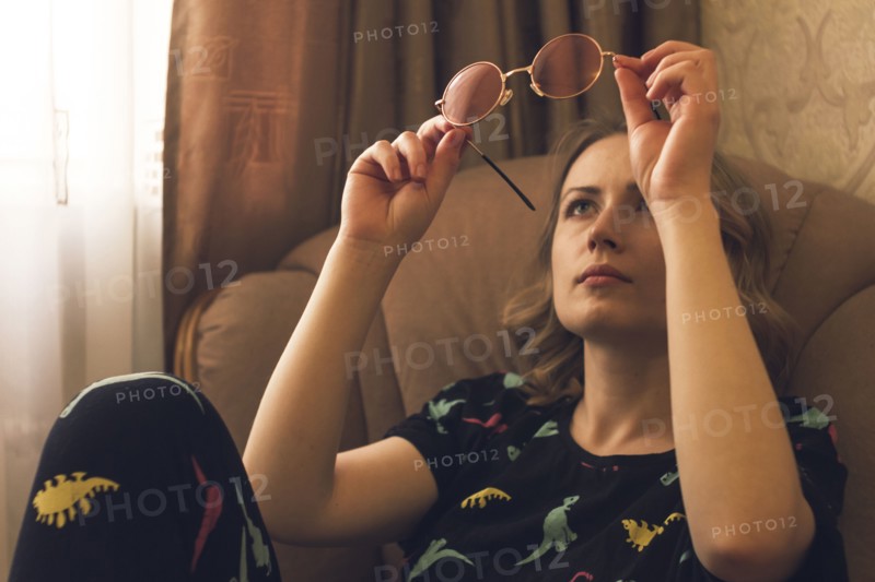Caucasian woman sitting in armchair examining sunglasses