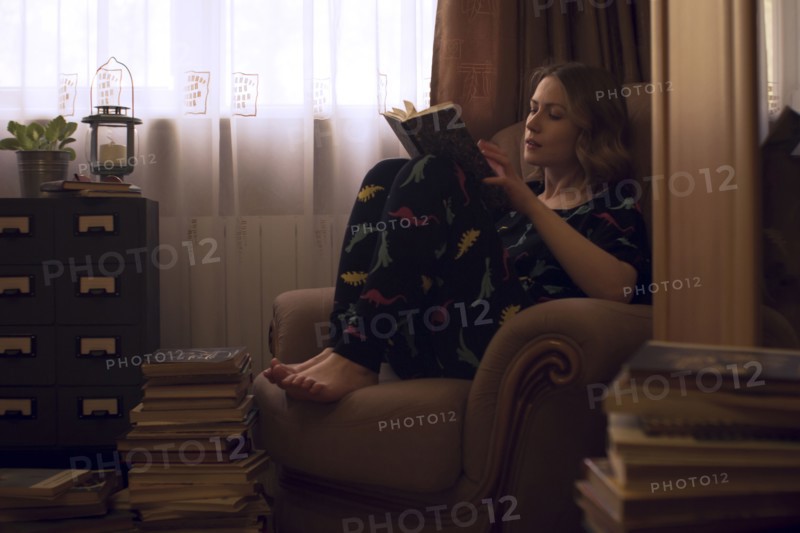 Caucasian woman sitting in armchair reading pile of books