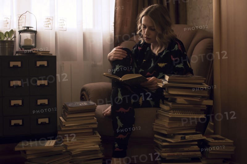 Caucasian woman sitting in armchair reading pile of books