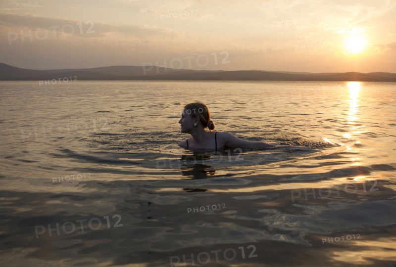 Caucasian woman swimming in lake at sunset