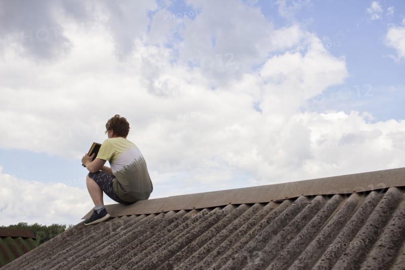 Caucasian man sitting on roof holding book