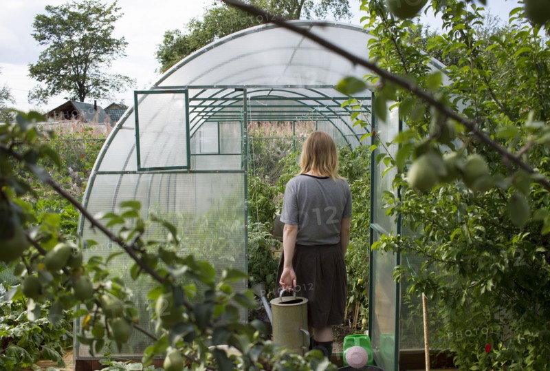 Caucasian woman carrying watering can to greenhouse