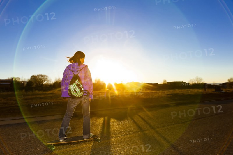 Chinese girl skateboarding on road at sunset