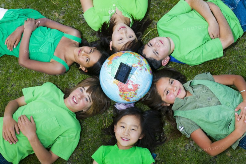 Children laying in grass around globe with solar panel