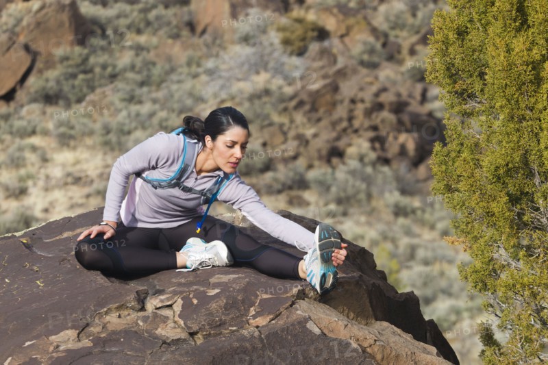 Hispanic woman stretching on rock