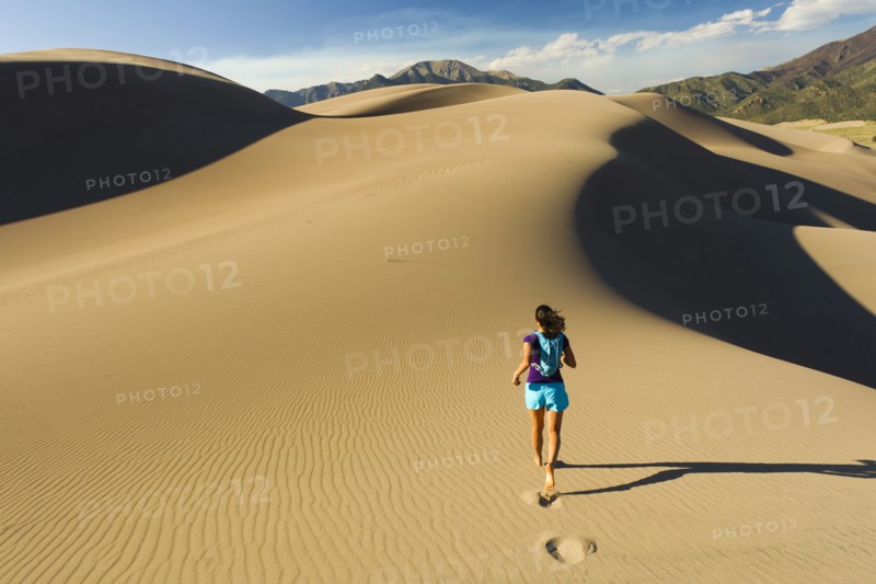 Hispanic woman running on sand dune