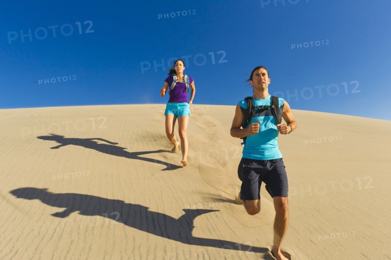 Hispanic couple running on sand dune