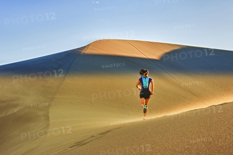 Hispanic woman running on sand dune