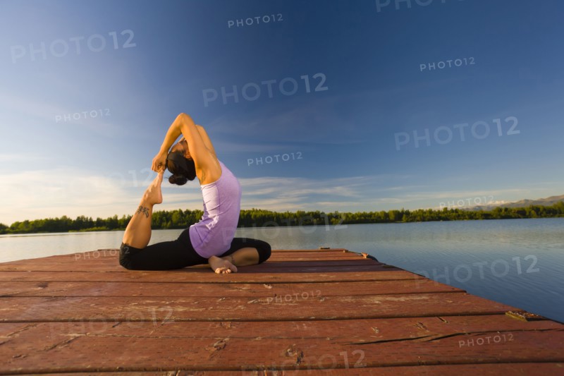 Korean woman practicing yoga on lake pier
