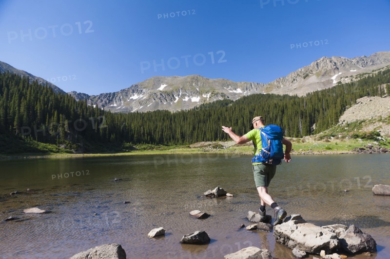Caucasian hiker climbing on rocks in lake