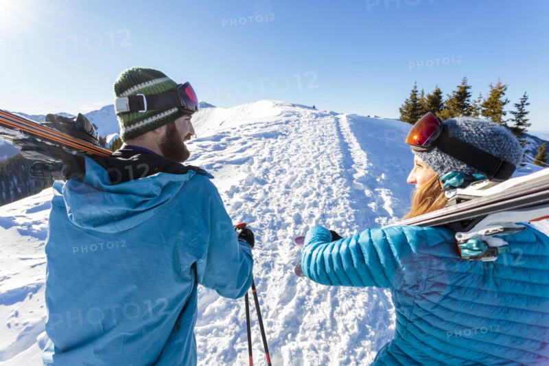 Couple carrying skis on snowy mountain