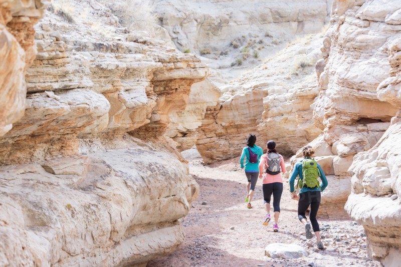 Women running in canyon wearing backpacks