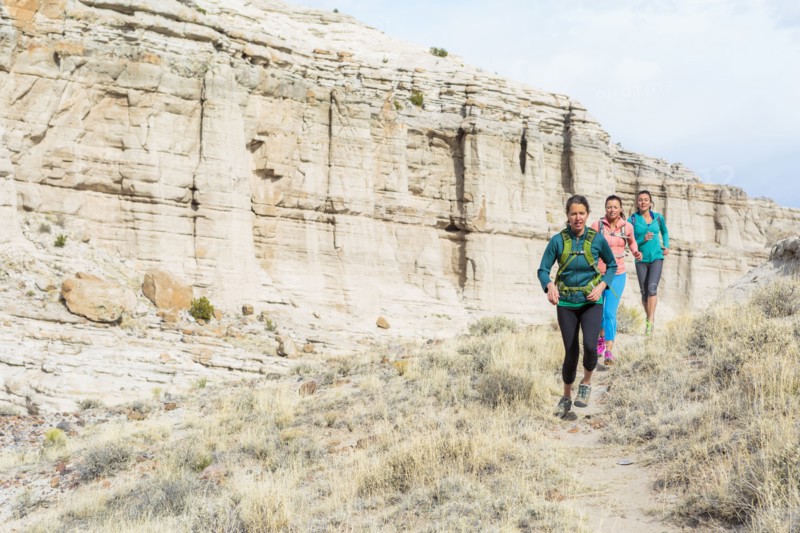 Women running in canyon wearing backpacks