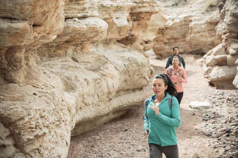 Women running in canyon wearing backpacks
