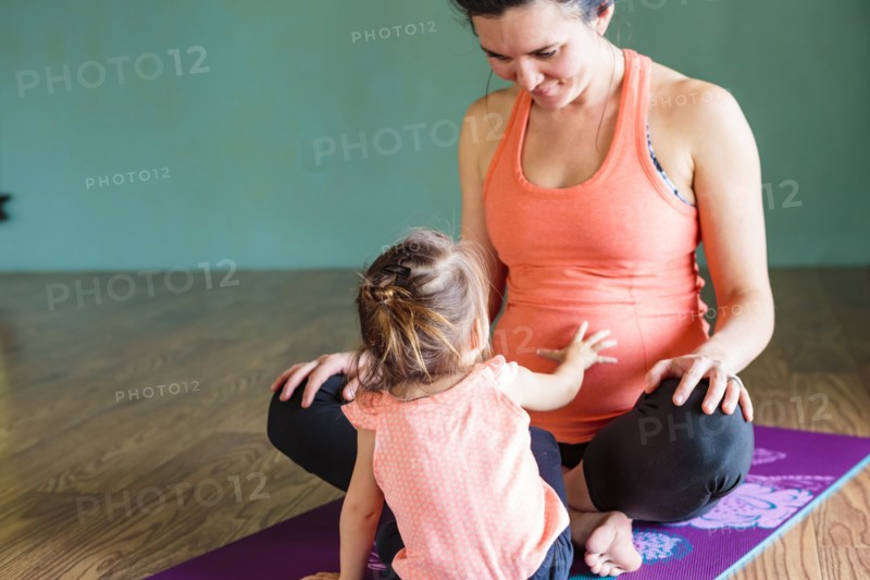 Mixed Race girl touching belly of expectant mother on exercise mat
