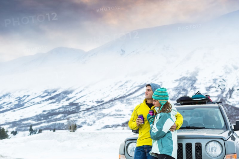 Caucasian couple hugging and leaning on car in winter