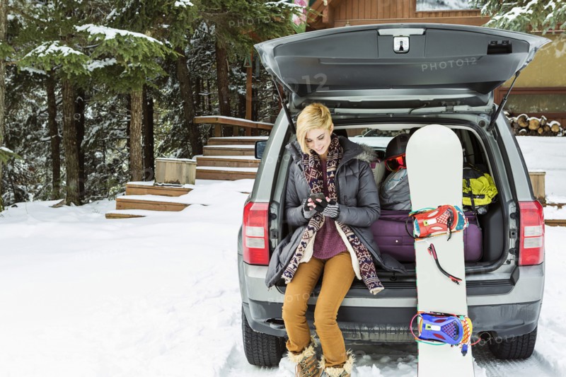 Caucasian woman at car texting on cell phone in winter