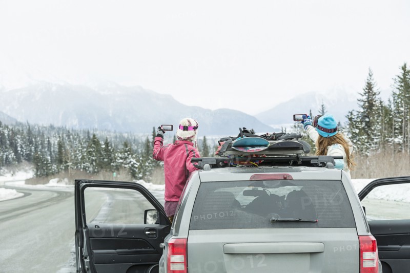 Caucasian women standing in car in winter photographing scenic view