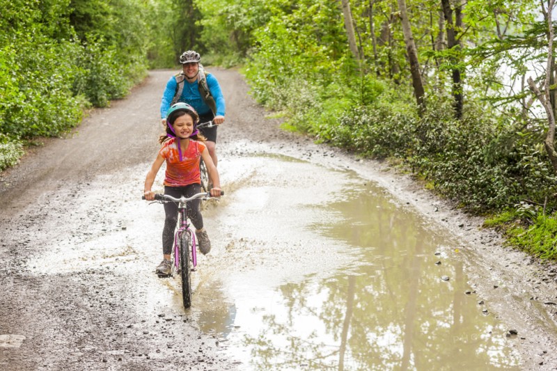 Father and daughter riding bicycles through puddle