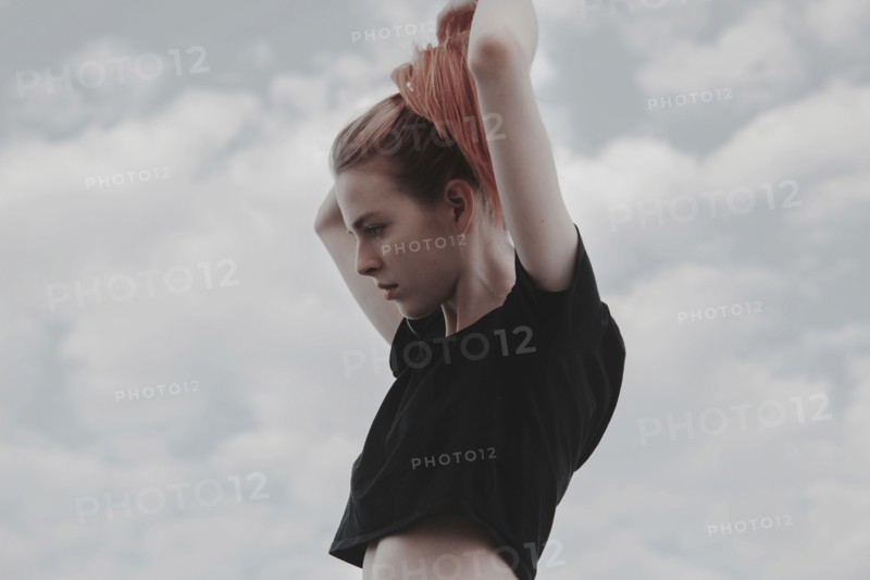 Caucasian woman arranging hair against clouds