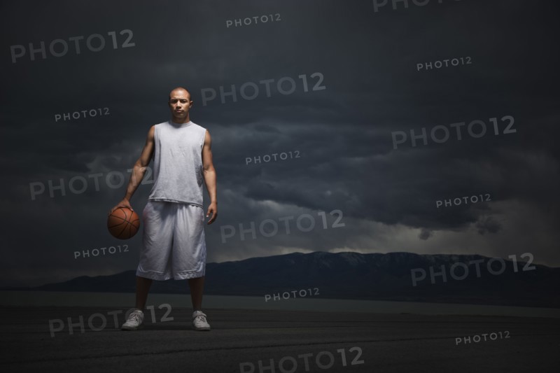 Mixed race basketball player standing with storm clouds in distance