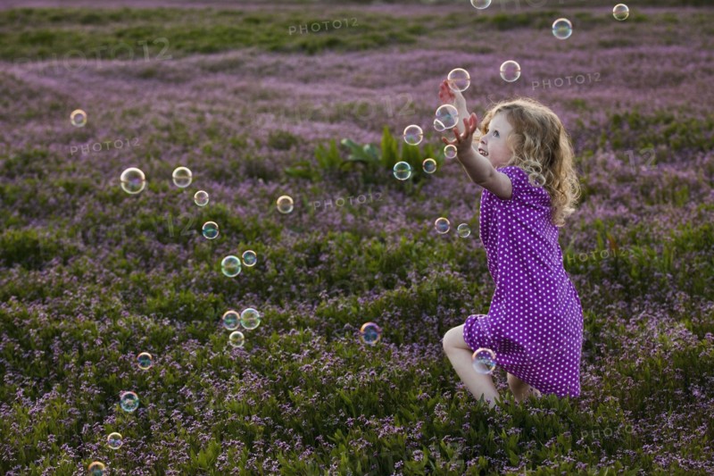 Caucasian girls chasing bubbles in field of flowers