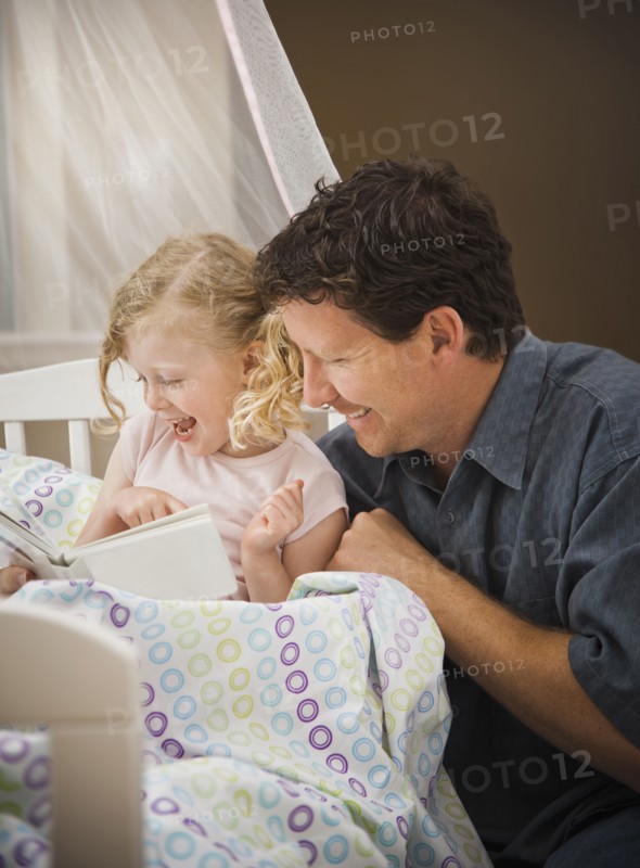 Caucasian father reading book to daughter in bed