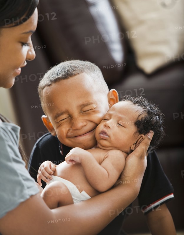 Mixed race boy hugging newborn baby