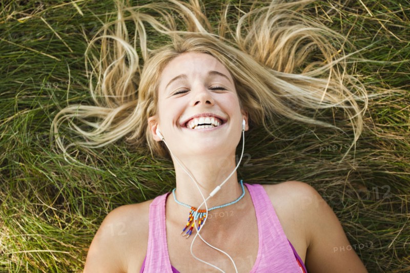 Caucasian woman laying in grass listening to music