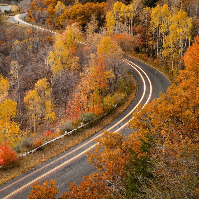 Long exposure of car driving on road through autumn leaves