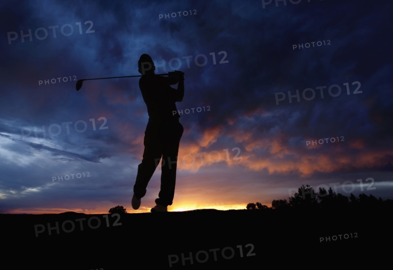 Caucasian golfer swinging golf club at sunset