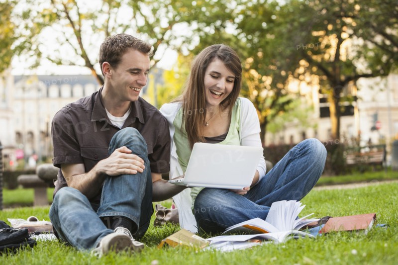 Caucasian students sitting in grass looking at laptop