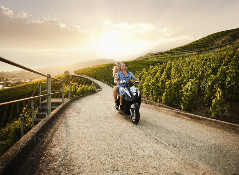 Couple riding scooter in vineyard